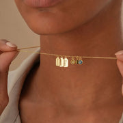 14k Gold necklace with name engraved charms and colorful gemstones held against a neutral background